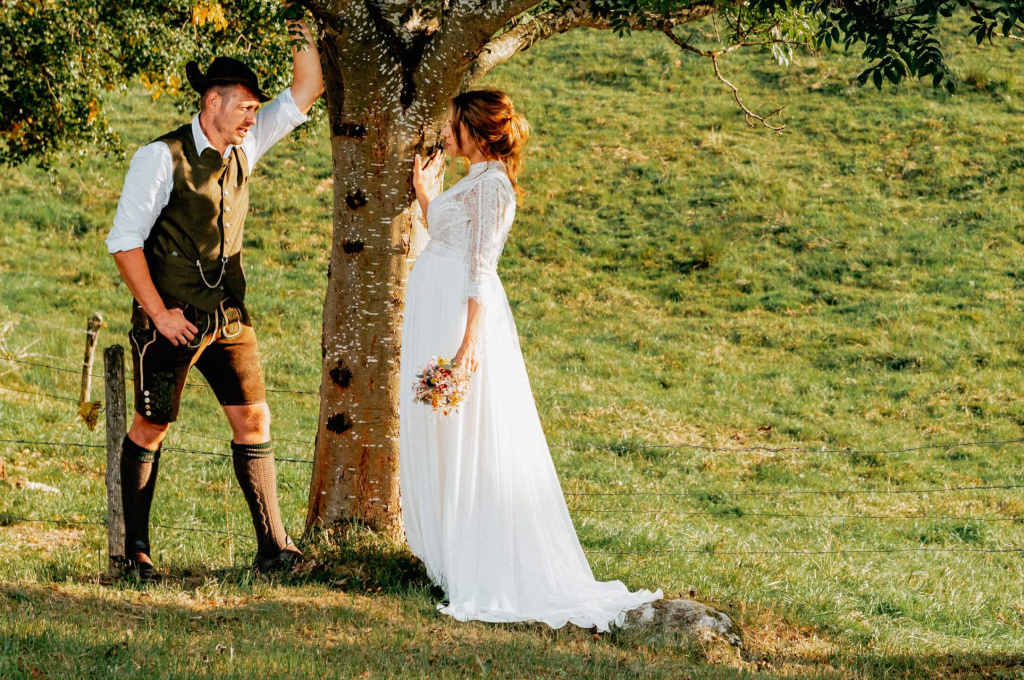 Hochzeitsfoto eines Paares unter einem Baum, im ländlichen Hintergrund mit Blumenstrauß.