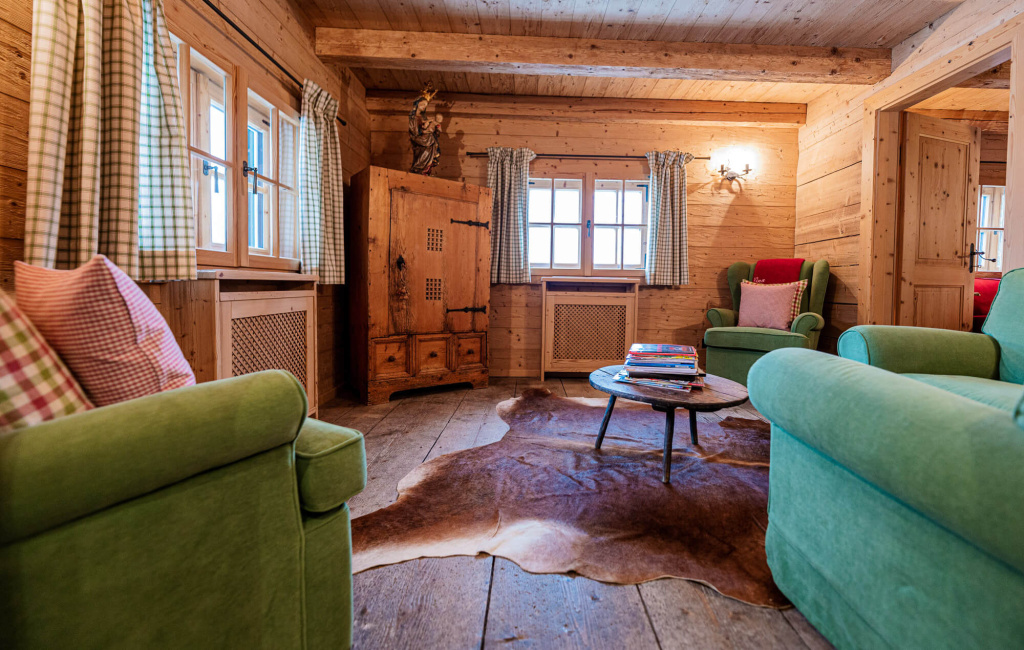 Gemütliche Holzstube mit grünen Sofas, Holzkamin und rustikaler Einrichtung.